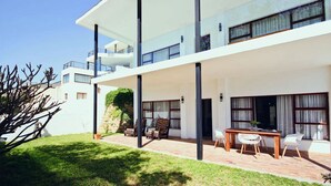 A modern two-story building with a covered patio area, outdoor seating, and a well-maintained lawn. - ADMIRAL'S COTTAGE (Cape Town)