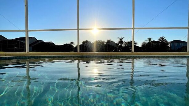 A clear swimming pool with a sunlit sky and distant palm trees. - Sunset Villa, Minutes from Disney. Exclusive 4 Bed, 2.5 Bath Pool Home (Kissimmee)
