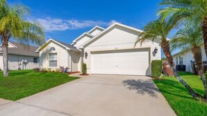 A two-story house with a white garage door, a well-maintained lawn, and palm trees. - Sunset Villa, Minutes from Disney. Exclusive 4 Bed, 2.5 Bath Pool Home (Kissimmee)