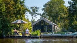 A dock with a wooden structure, a boat, and a person fishing. - Nature lodge Blaukopke, Akkrum - private jetty, sleeps 6 (Akkrum)