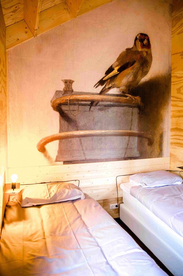 A room with two beds, a wooden ceiling, and a wall mural of a bird.