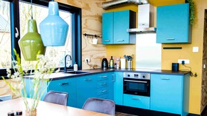 A modern kitchen with blue cabinets, a wooden dining table, and a window with a view of trees. - Nature lodge Blaukopke, Akkrum - private jetty, sleeps 6 (Akkrum)