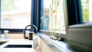 Una encimera de cocina con una tetera, una botella y un ventanal con vistas a la vegetación.