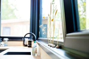 Un plan de travail de cuisine avec une bouilloire, une bouteille et une fenêtre donnant sur un paysage verdoyant.