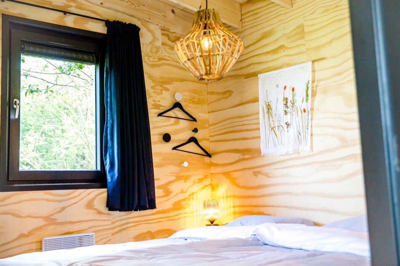 Ein Schlafzimmer mit Bett, einem Fenster mit Vorhängen, einer Wandleuchte und einem Wandbild.