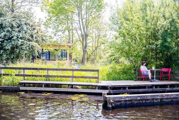 A wooden dock extending over a body of water with a person sitting at a table and a bench nearby. - Nature lodge Iisfûgel, Akkrum - 2 bathrooms, sleeps 4 (Akkrum)