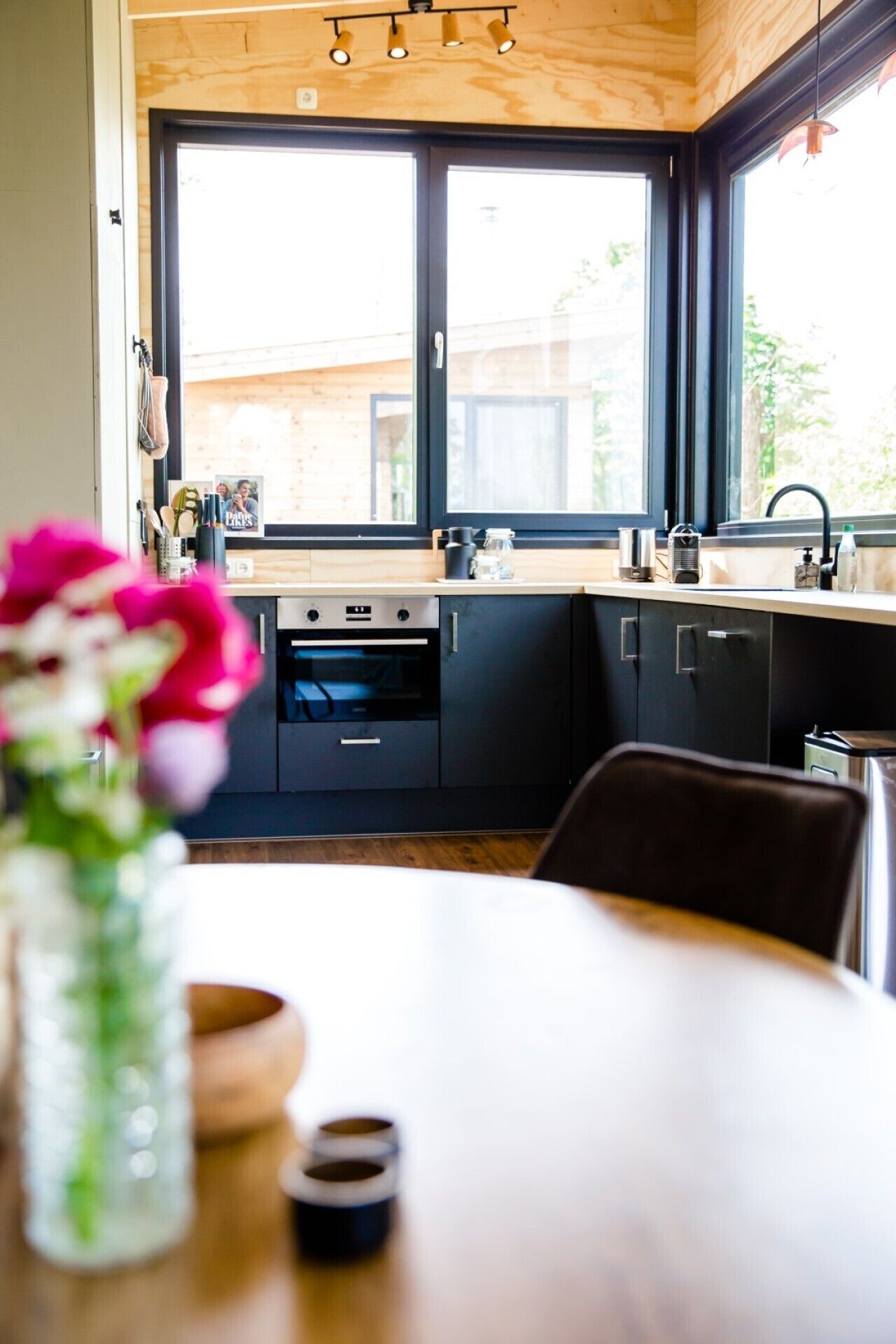 Une cuisine moderne dotée d’une grande fenêtre, de meubles de rangement aux couleurs sombres et d’un plafond en bois.
