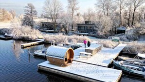 Ein Winterbild mit einem am Kai liegenden Boot, einer hölzernen Struktur mit einer Bank und einem Gebäude im Hintergrund.