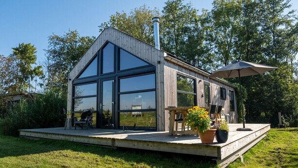 Eine moderne Holz-Blockhütte mit großen Glasfenstern, einer Terrasse und Sitzgelegenheiten im Freien.