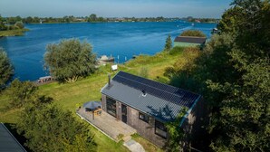 Ein modernes Haus mit Solardach, das auf einem grasbewachsen Hügel mit Blick auf einen See liegt.
