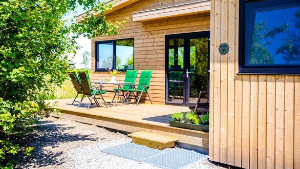 A wooden cabin with a deck, green chairs, and a small garden area. - Nature lodge Sweltsje, Akkrum - sleeps 4 by the water (Akkrum)