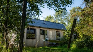 A wooden cabin with a metal roof, surrounded by lush greenery and trees. - Nature lodge Skries, Akkrum - sleeps 8, 3 bedrooms (Akkrum)