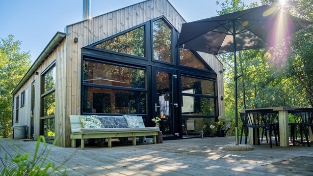 A modern wooden building with large glass windows, a bench, and a table with chairs outside. - Nature lodge Skries, Akkrum - sleeps 8, 3 bedrooms (Akkrum)