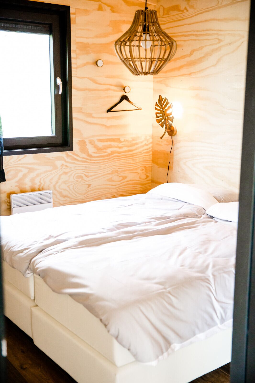 A bedroom with a bed, a hanging light fixture, and a wall-mounted plant.