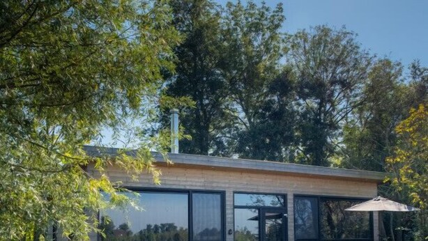 Een modern huis met een terras, buitenmeubels en een groot raam met uitzicht op een gazon.
