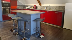 Une cuisine moderne avec des meubles de couleur rouge, un îlot central doté de tabourets de bar, des appareils en acier inoxydable et un plafond en bois.