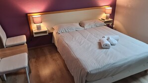 Un lit bien fait, avec du linge de lit blanc et deux oreillers, une table de chevet avec une lampe et une chaise.