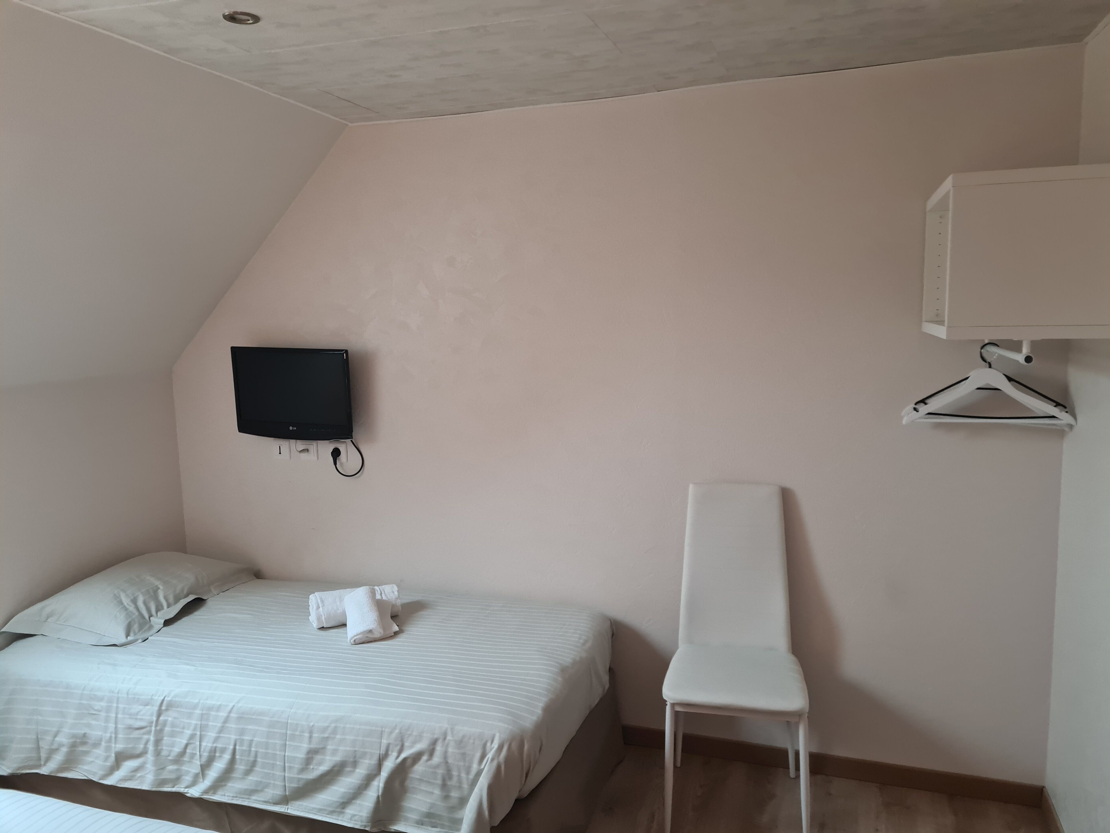 A bedroom with a bed, a TV mounted on the wall, a white chair, and a white wardrobe.