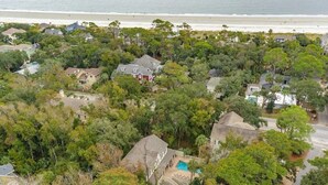 Vue aérienne d’un quartier résidentiel, avec des maisons entourées d’une végétation luxuriante, une piscine et une plage en arrière-plan.
