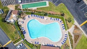 Vue aérienne d’une piscine avec des chaises longues, un espace abrité et un parking.