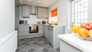 A modern kitchen with grey cabinets, a dishwasher, and a fruit bowl on the counter. - HC Property - The Old Clubhouse (Bishop Auckland)