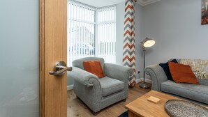 A room with a grey armchair, a sofa, a wooden coffee table, and a floor lamp. - HC Property - The Old Clubhouse (Bishop Auckland)