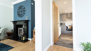 A modern living room with a fireplace, a clock on the wall, and a view into the kitchen through an open door. - HC Property - The Old Clubhouse (Bishop Auckland)