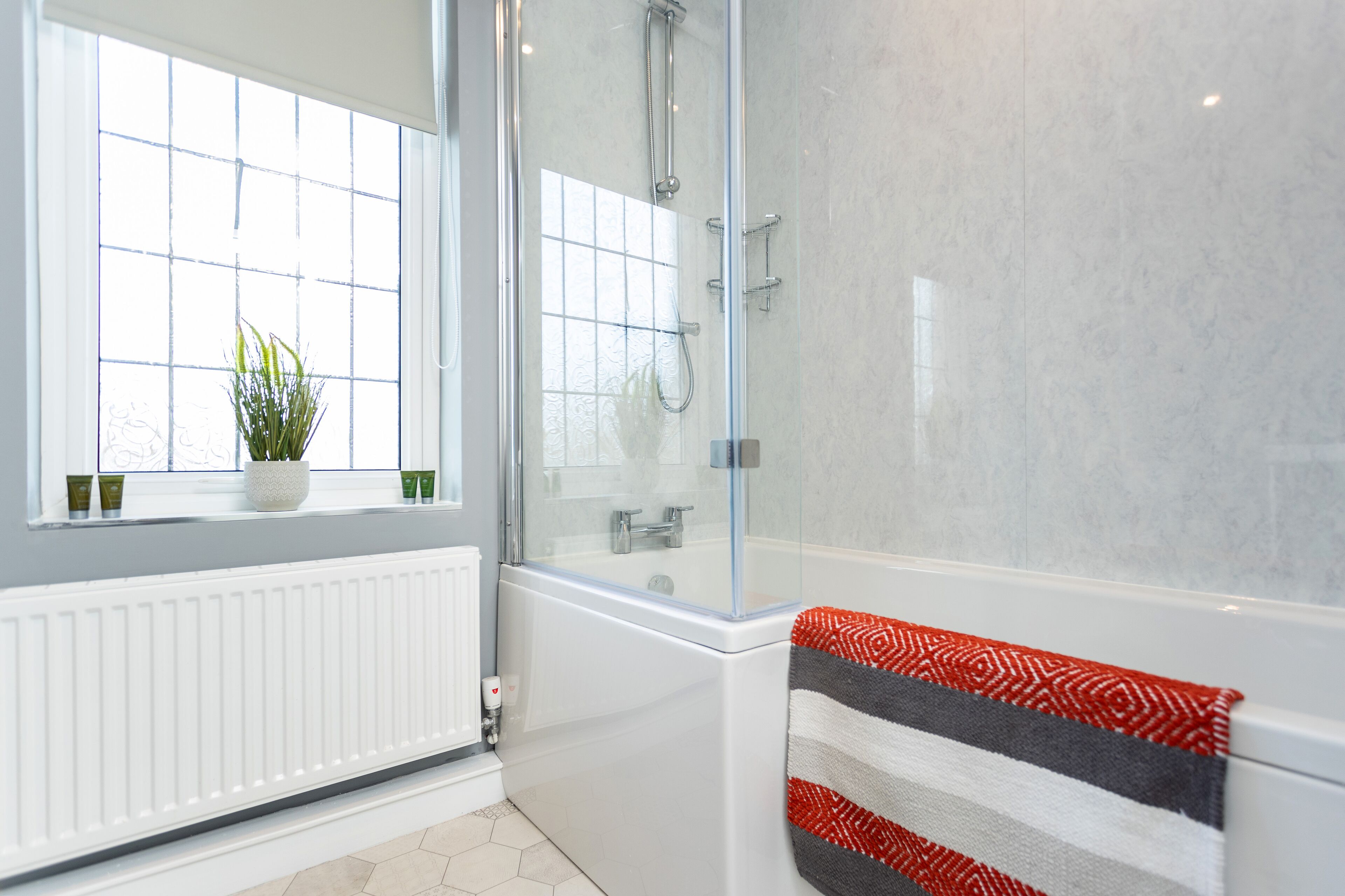 Ein modernes Badezimmer mit einer gläsernen Dusche, einer weißen Badewanne und einem Fenster mit einem Blumentopf.
