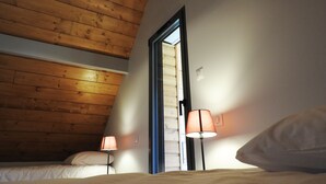 A bedroom with wooden ceiling beams, a bed with white bedding, two bedside lamps, and a door leading to another room. - Chalet Viscos (Les Chalets du Balandrau) (Ayzac-Ost)