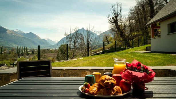 A breakfast table with croissants, strawberries, a teddy bear, and a bouquet of roses, set against a scenic mountain backdrop. - Chalet Viscos (Les Chalets du Balandrau) (Ayzac-Ost)