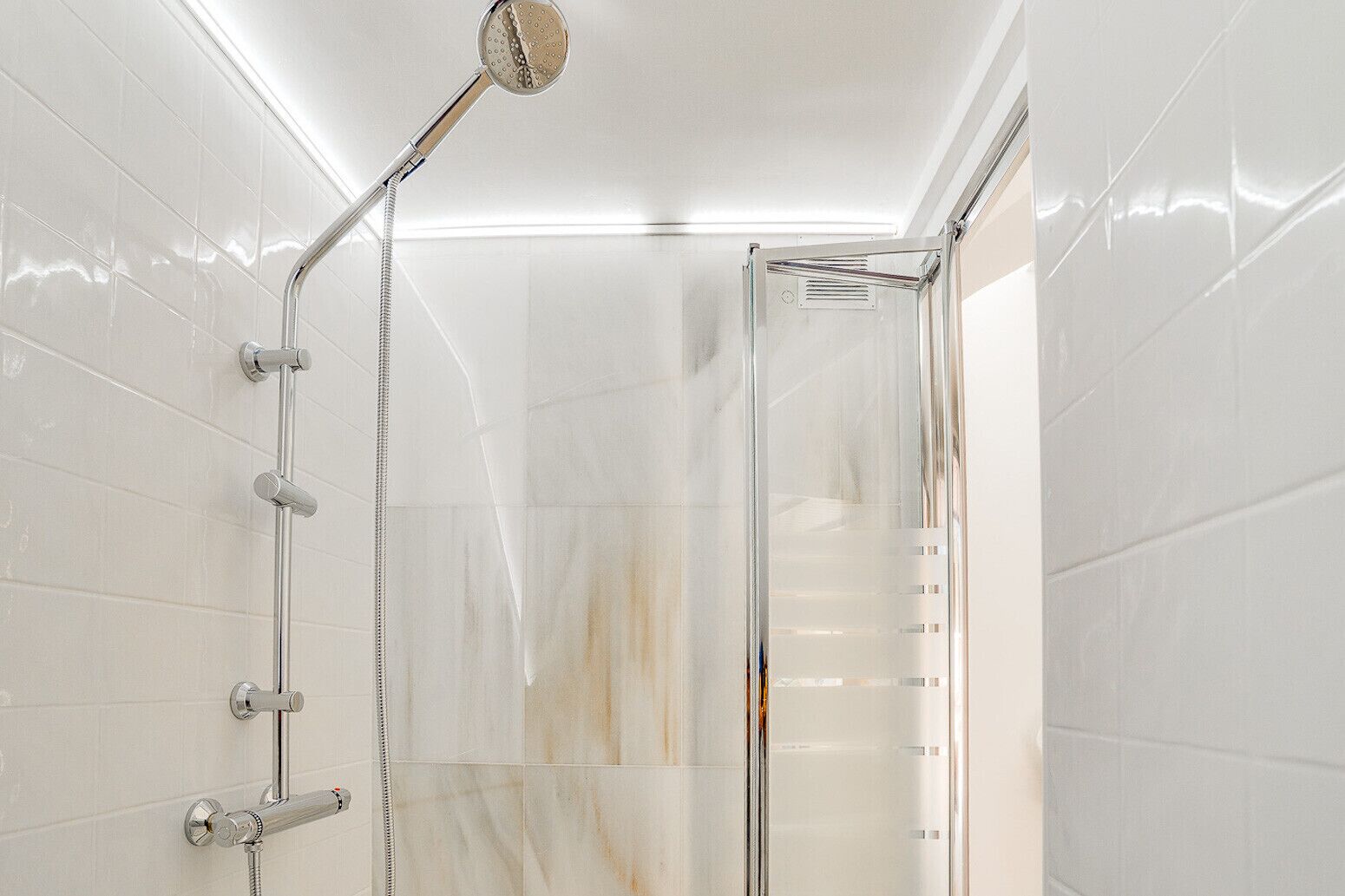 Une douche moderne avec un pare-douche en verre, des robinetteries chromées et un éclairage au plafond.