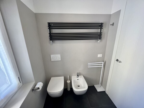 Une salle de bain moderne équipée d’un WC, d’un bidet, d’un porte-serviettes et d’un support à papier toilette.