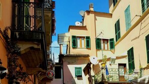 A narrow street with buildings on either side, a pedestrian underpass, and outdoor seating areas. - Family Room inside the Guesthouse on the Arch (Monterosso al Mare)