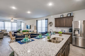 A modern kitchen with granite countertops, stainless steel appliances, and a dining area with blue placemats and green centerpieces.