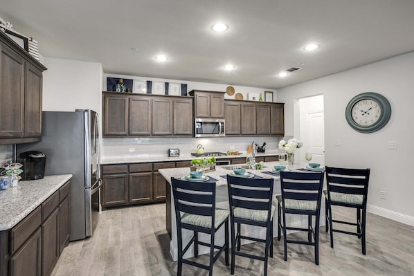 A modern kitchen with dark wood cabinets, a stainless steel refrigerator, a microwave, and a dining area with four chairs and a table set for four.