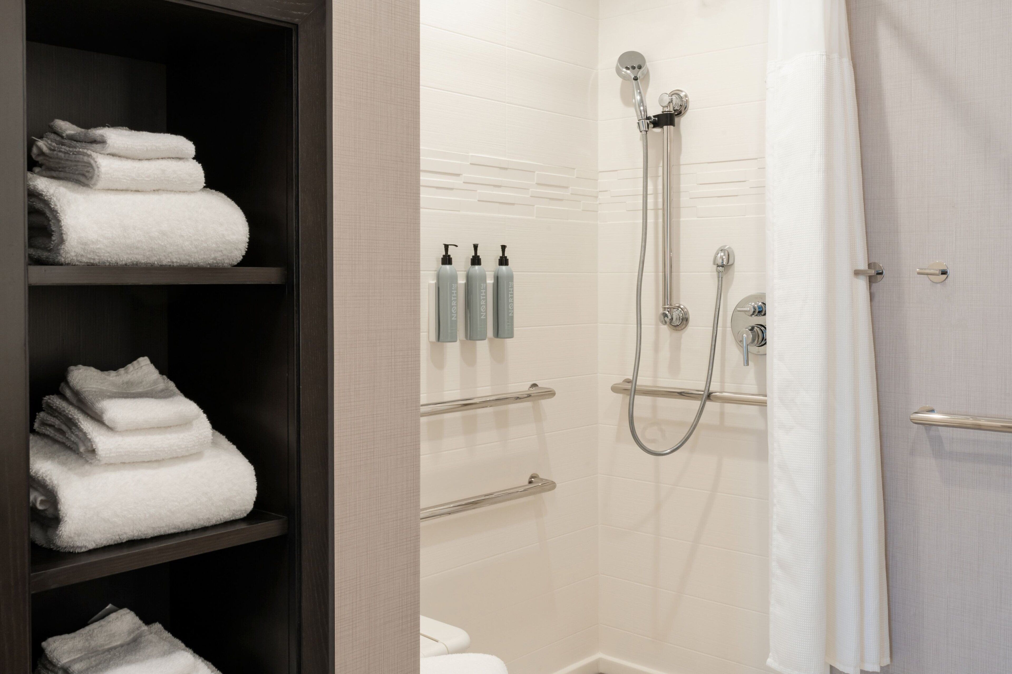 Une salle de bain avec une douche, des toilettes et des étagères où sont rangées les serviettes.