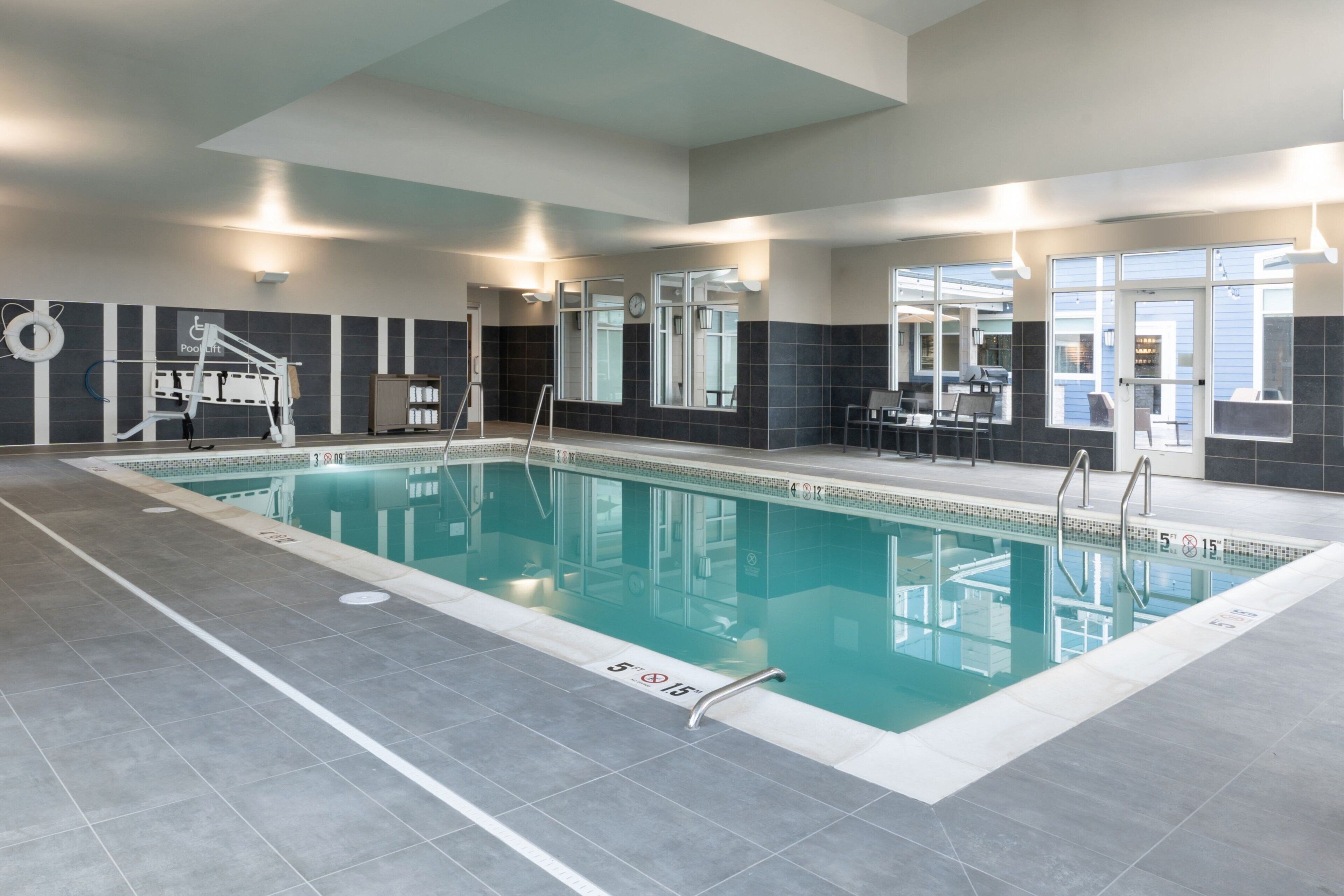 A modern indoor swimming pool with clear lane markings, a lifeguard chair, and a poolside seating area.