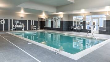 A modern indoor swimming pool with clear lane markings, a lifeguard chair, and a poolside seating area.