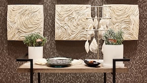 A modern bathroom with a textured wall, a towel rack, two potted plants, a glass bowl, and a black bowl on a wooden table. - AC Hotel Atlanta Perimeter (Atlanta)