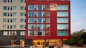 A modern hotel with a red and beige facade, multiple windows, and a visible entrance with outdoor seating. - AC Hotel Atlanta Perimeter (Atlanta)