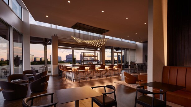 A modern interior with a bar area, seating, and large windows offering city views. - AC Hotel Atlanta Perimeter (Atlanta)