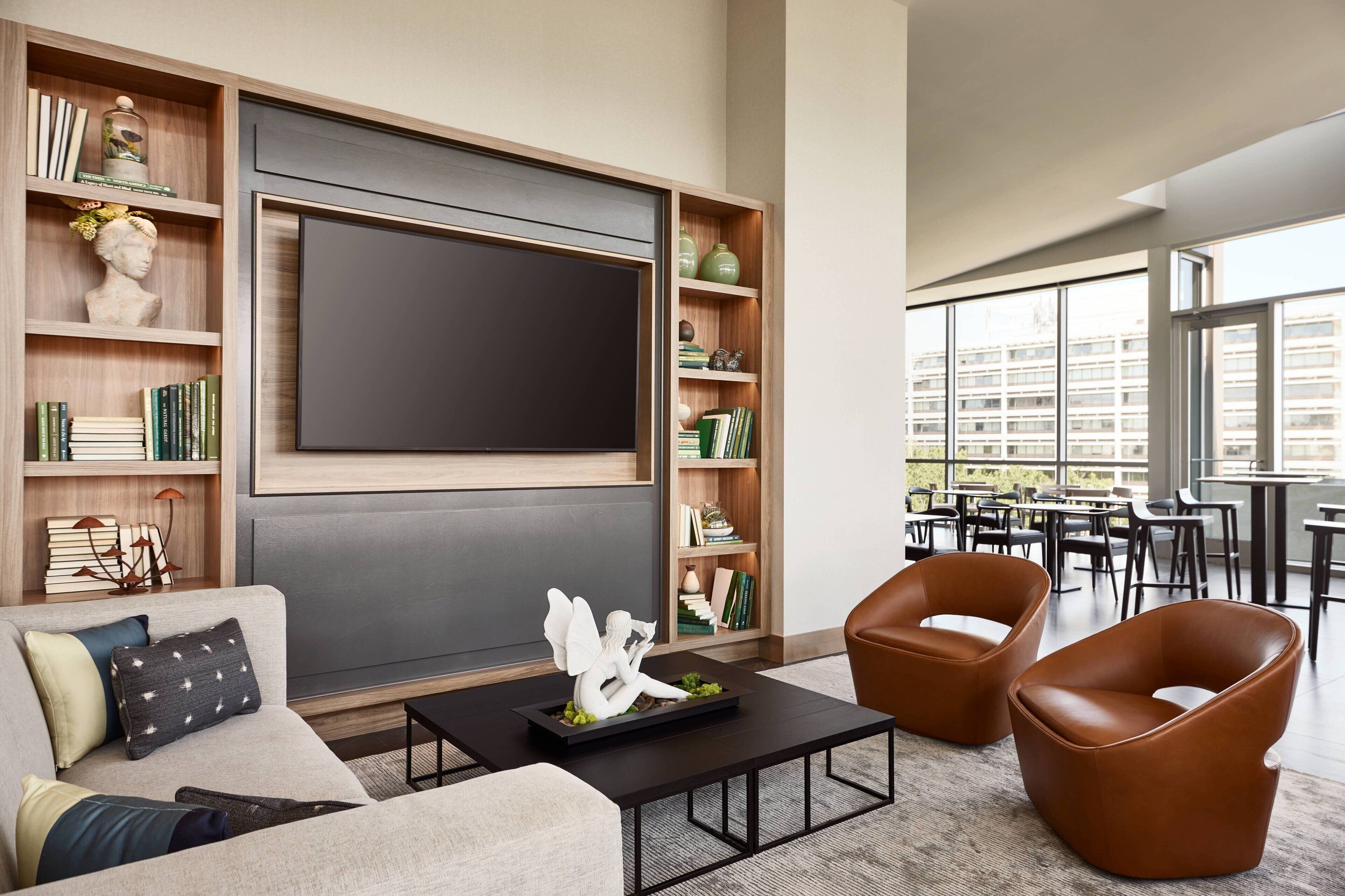 A modern living room with a large flat-screen TV, built-in bookshelves, a sofa, two leather armchairs, and a coffee table.
