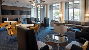 A modern hotel lobby with a mix of seating areas, including a sofa, chairs, and a round table. There are large windows providing natural light and a view of the outside. - Courtyard by Marriott Fresno Clovis (Clovis)