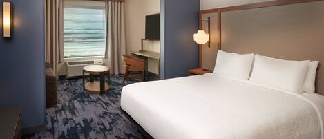 A hotel room with a large bed, a desk, a chair, a TV, and a window with curtains.