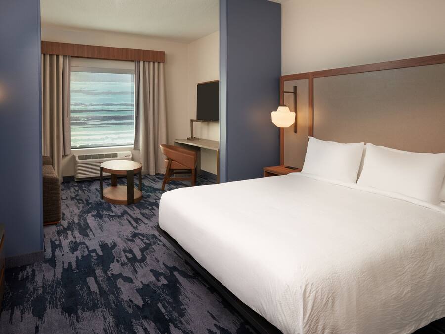 A hotel room with a large bed, a desk, a chair, a TV, and a window with curtains.