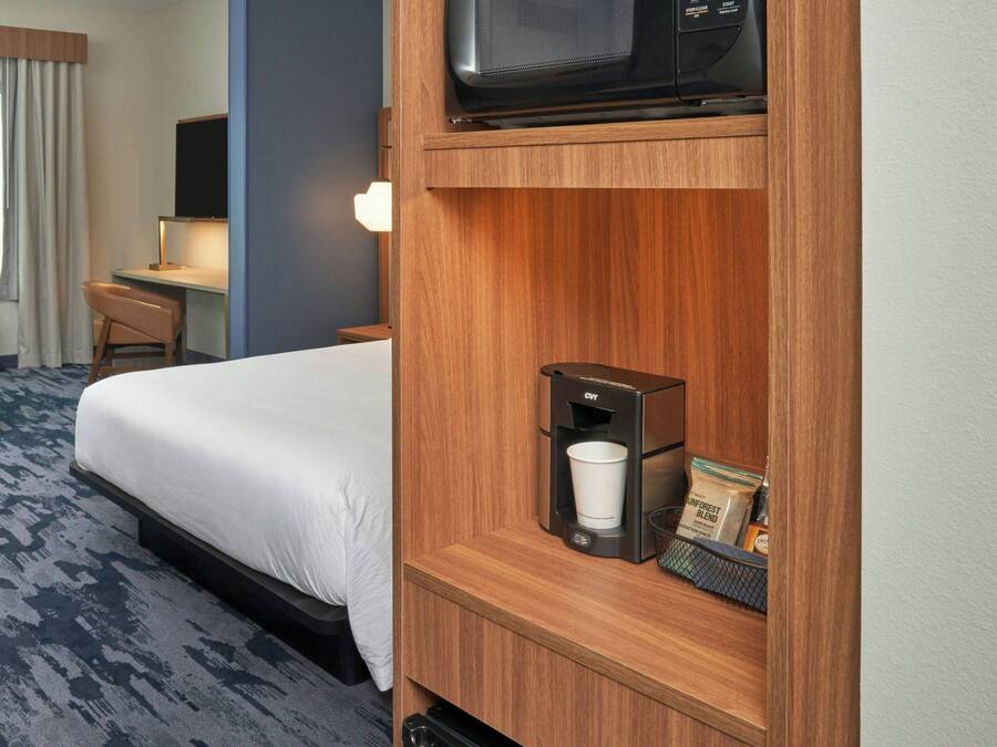 A hotel room with a bed, a desk with a chair, a television, a coffee maker, and a window with curtains.