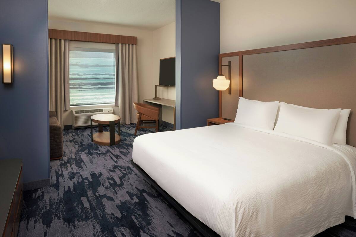 A hotel room with a large bed, a desk, a chair, a TV, and a view of the ocean.