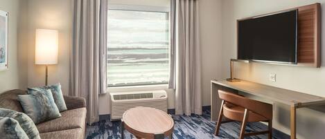 A hotel room with a large window, a sofa, a desk, and a chair.