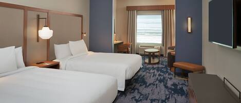 Quarto de hotel com duas camas, uma escrivaninha, uma cadeira, uma televisão e uma janela com vista para o oceano.