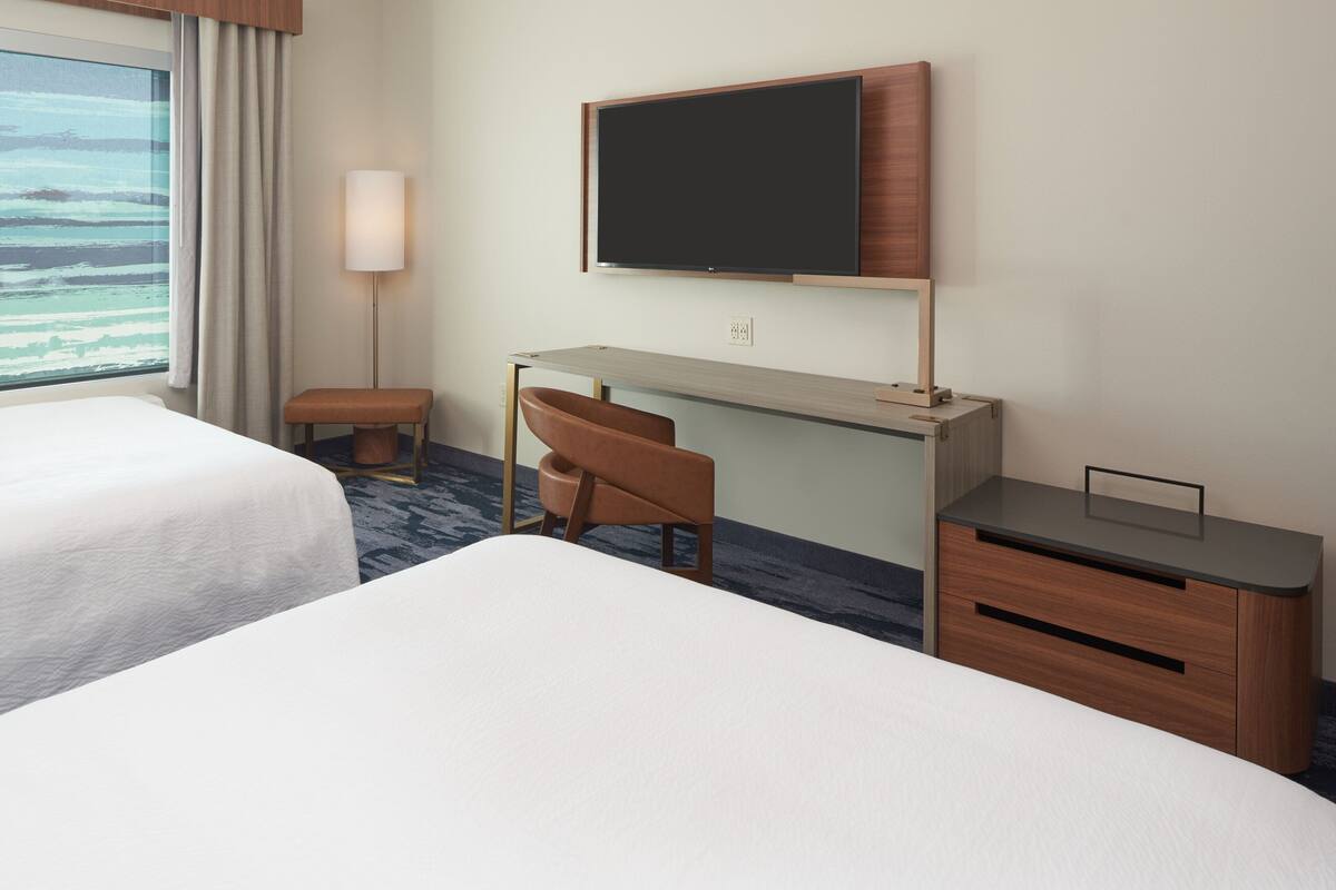A hotel room with two beds, a desk, a chair, a TV, and a window with curtains.